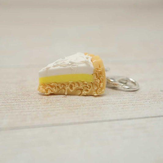 Keychain shaped like a slice of cake with white frosting and yellow filling on a light wooden surface | Market Town Yarns
