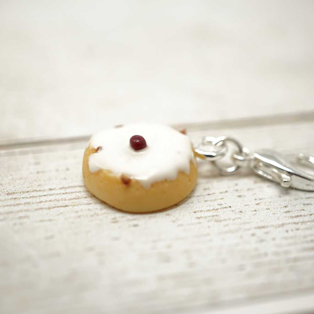 Donut-shaped keychain with white icing and a red berry on a light wooden surface | Market Town Yarns