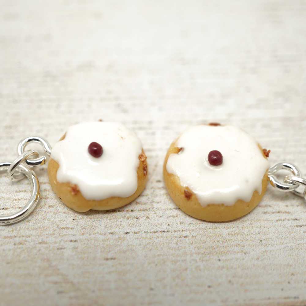 Two small keychain charms shaped like donuts with white icing and a red berry on a light wooden surface | Market Town Yarns