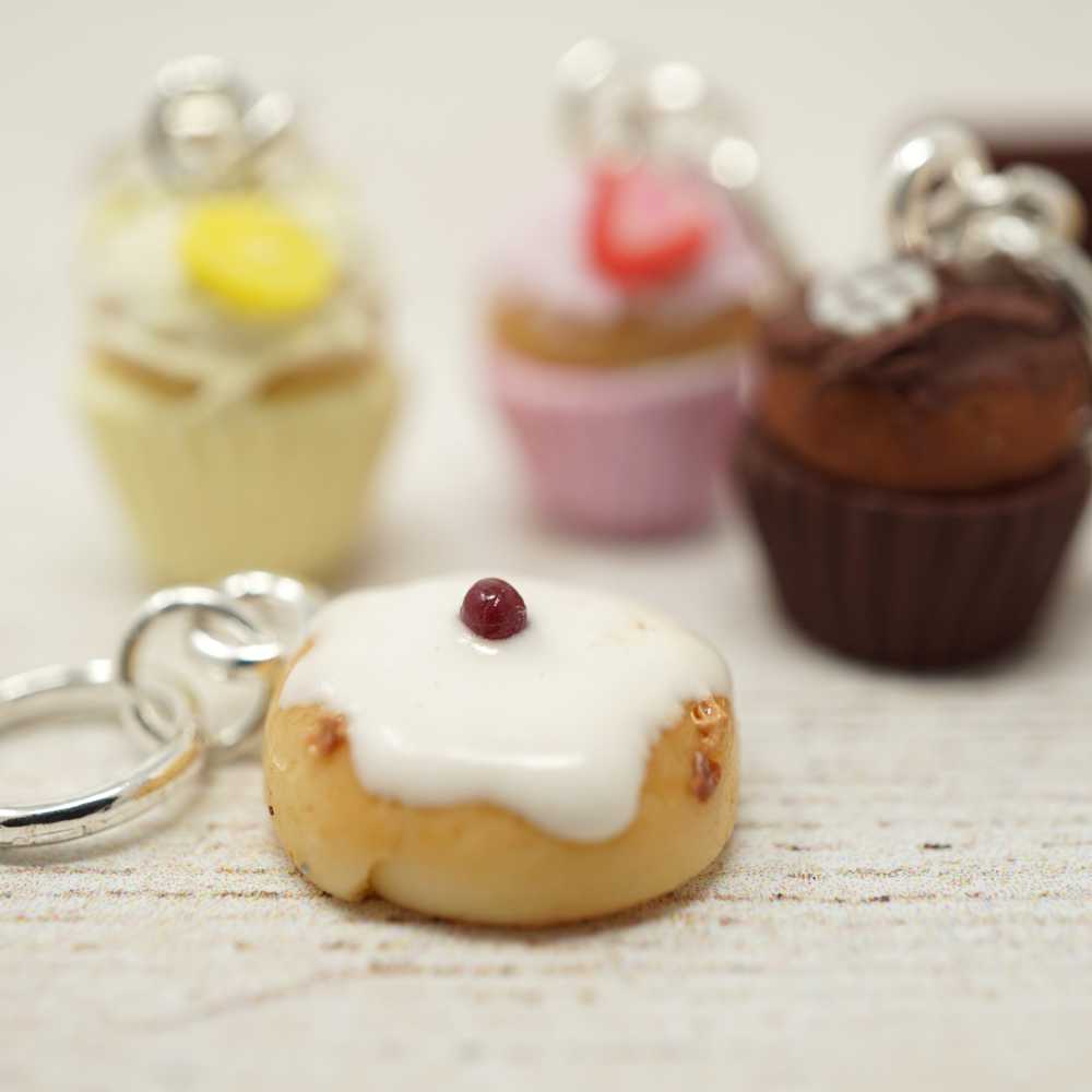 Close-up of a keychain shaped like a small cake with white frosting and a red cherry on top, with other similar keychains in the background | Market Town Yarns