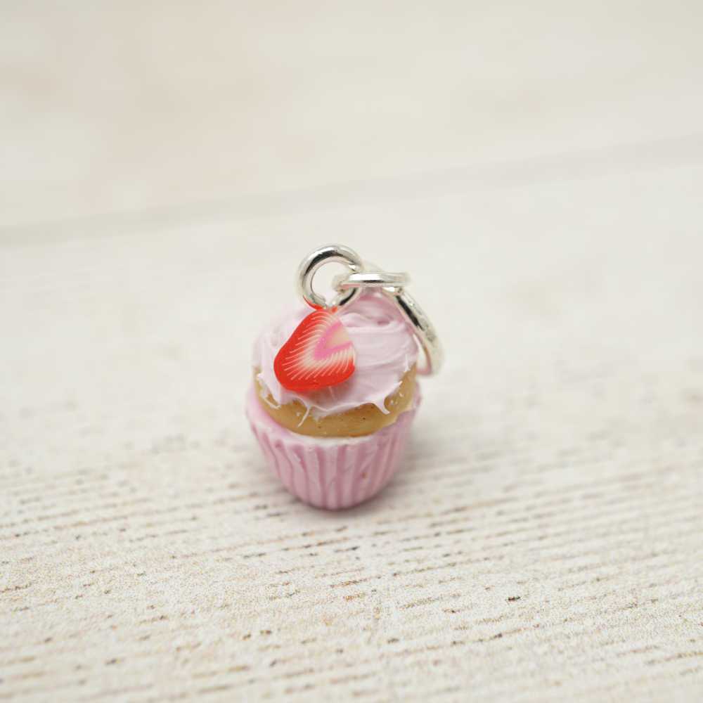 Cupcake charm with a red cherry on top on a textured beige surface | Market Town Yarns