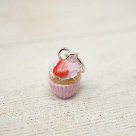 Cupcake charm with a red cherry on top on a textured beige surface | Market Town Yarns